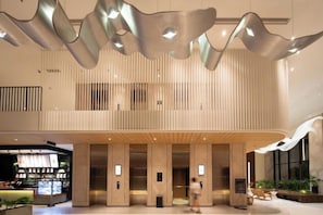 Un hall d’entrée spacieux au design moderne, doté d’un plafond haut, d’une colonne centrale et d’un espace salon offrant une vue sur l’intérieur.