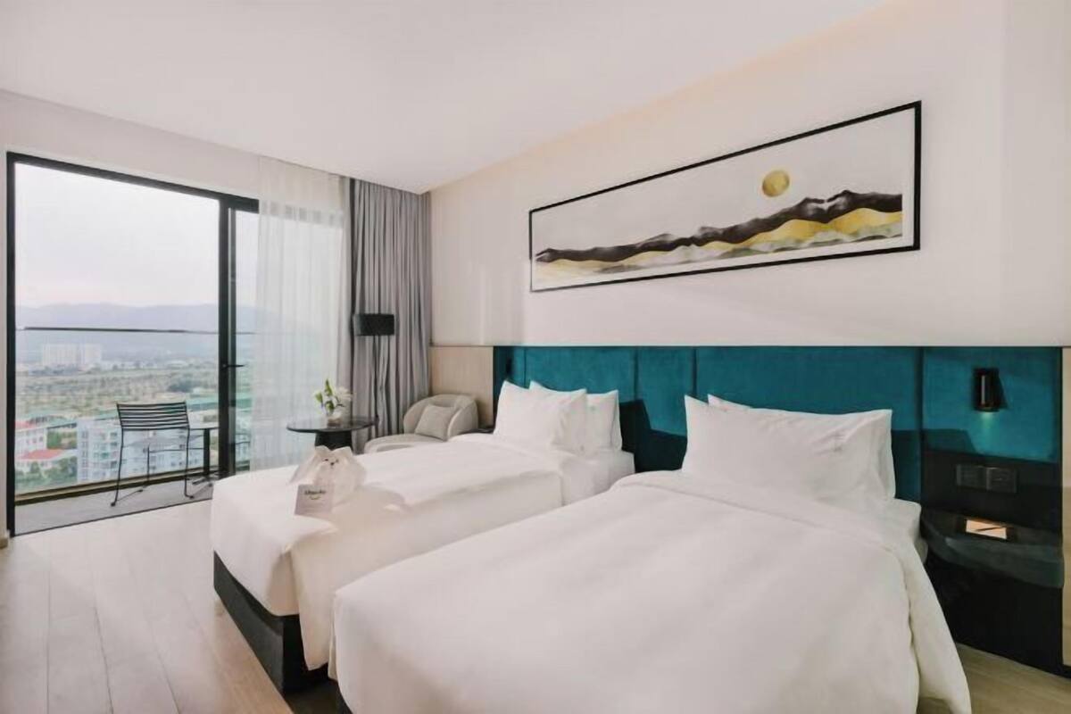 A hotel room with two beds, a city view, a painting on the wall, and a desk with a chair.