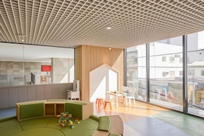 A modern interior with a high ceiling, a seating area with a play table, and large windows offering a view of the city. - December Hotel (Nha Trang)