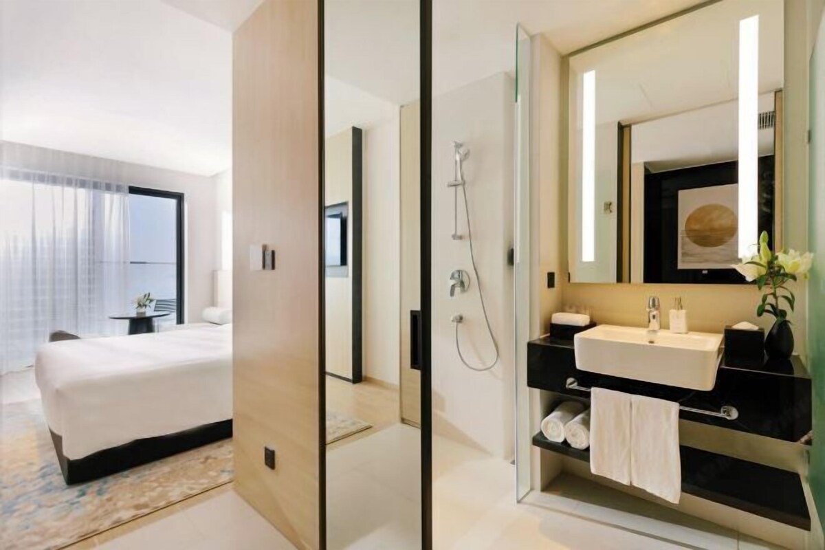 A modern hotel room with a large bed, a bathroom with a mirror, sink, and towel rack.