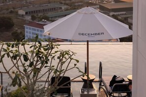 A balcony with a white umbrella labeled 'DECEMBER HOTEL,' a table, chairs, and a view of the surrounding area. - December Hotel (Nha Trang)