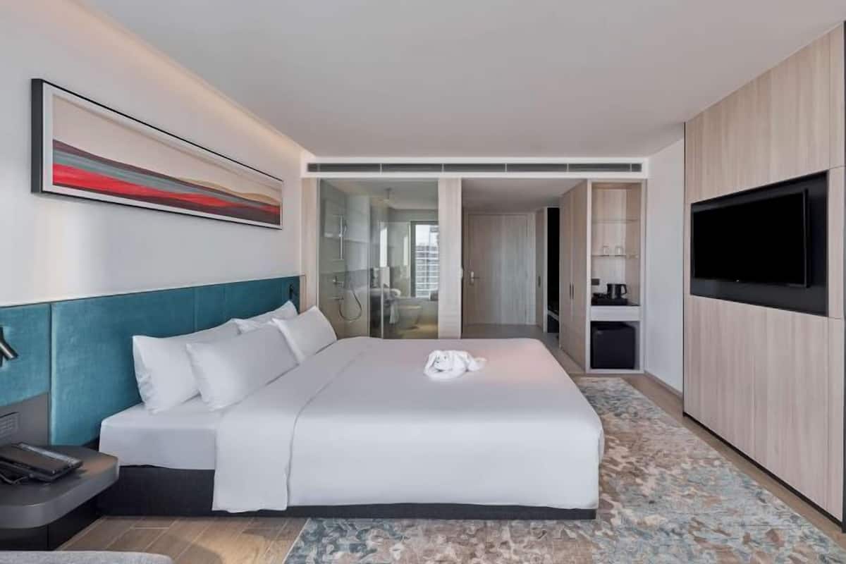 A modern hotel room with a large bed, a flat-screen TV, a desk with a phone, and a painting on the wall.