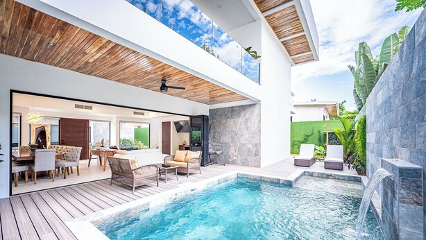 Ein moderner Poolbereich im Freien mit Holzterrasse, Liegestühlen und einem Wasserfall.