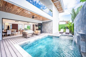 Un área de piscina moderna al aire libre con terraza de madera, sillones de descanso y una cascada.