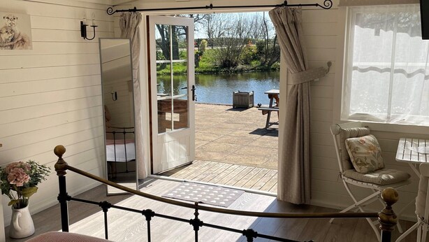 A bedroom with a large bed, a view of a garden through an open door, a chair, and a table. - Wethele Manor (Royal Leamington Spa)