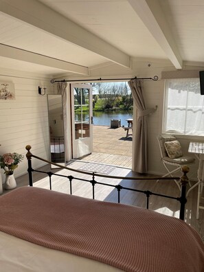 A bedroom with a large bed, a view of a garden through an open door, a chair, and a table. - Wethele Manor (Royal Leamington Spa)