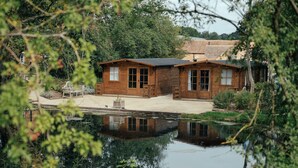 A wooden cabin with a pond in front, surrounded by trees. - Wethele Manor (Royal Leamington Spa)