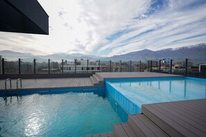 Piscina no terraço com vista para a cidade e montanhas ao fundo.
