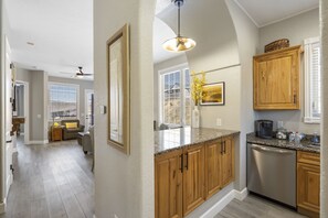 Enjoy cooking in this well-equipped kitchen with a dishwasher and coffee maker, adjacent to a dining area with a sofa and small table.