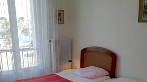 A bedroom with a bed, a radiator, a window with curtains, and a view of the outside.