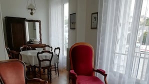 A spacious living room with wooden flooring, a glass coffee table, and a red armchair. There is a dining area with a table and chairs in the background.