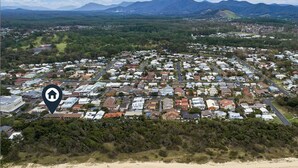 Vue aérienne d’une zone résidentielle côtière, avec des maisons, une plage et des montagnes en arrière-plan.