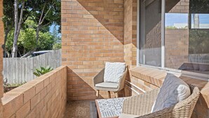 Un espace extérieur lumineux, aménagé pour s’asseoir, avec des murs en briques, une chaise en osier et un banc rembourré.