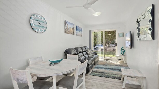 Un salon moderne avec un canapé blanc, une table à manger avec des chaises, une grande horloge et des œuvres d’art accrochées aux murs.