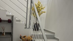 Eine Treppe mit Metallgeländer, ein Blumentopf mit gelben Blüten und ein Regal mit Dekoration.
