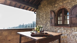 A rustic wooden table with wine bottles and glasses, set against a stone wall with arched windows. - Borgo La Collina (Verona)