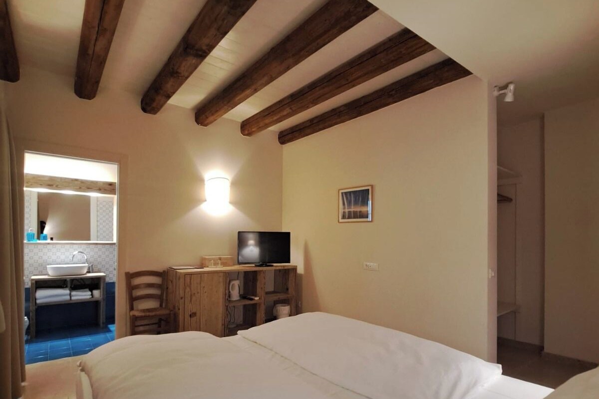 A bedroom with a large bed, wooden beams on the ceiling, a television on a wooden stand, and a small table with a chair.