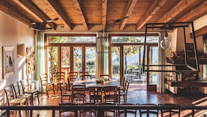 A dining area with wooden tables and chairs, large windows with curtains, and a view of the outdoors. - Borgo La Collina (Verona)