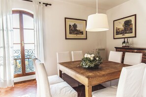 Une salle à manger avec une table en bois, des chaises blanches, un arrangement floral en guise de centre de table et deux tableaux encadrés accrochés au mur.