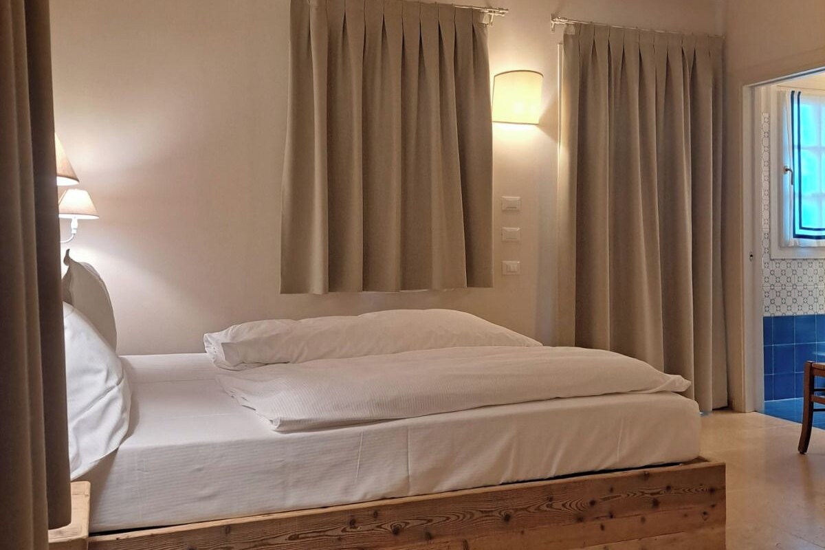 Een slaapkamer met een houten bed, een nachtkastje, een lamp en een raam met gordijnen.