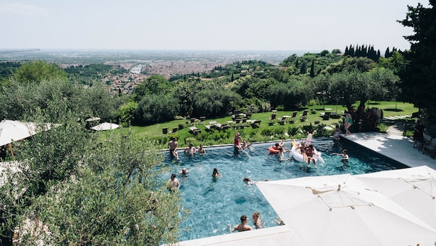 A swimming pool surrounded by lush greenery and a view of a distant cityscape. - Borgo La Collina (Verona)
