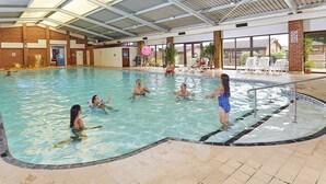 Una piscina interna con acqua cristallina, circondata da poltroncine relax e una struttura coperta.