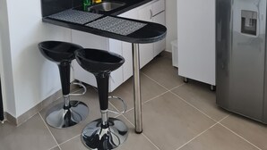 A modern kitchen with a black countertop, two bar stools, a refrigerator, and pendant lights. - 402 Moderno Aparta-Suite en Versalles Tipo Loft - Cali Tower Suites & Lofts (Cali)