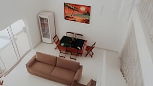 Un vaste espace de vie comprenant un grand canapé, une petite table et des chaises. Un tableau orne le mur et une fenêtre laisse entrer la lumière naturelle.