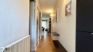 Ein schmaler Flur mit Heizkörper, einem schwarzen Kühlschrank und einem Essbereich in der Ferne.