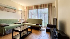Ein Wohnzimmer mit zwei Sofas, einem Couchtisch, einem Fernseher und einem Fenster mit Vorhängen.