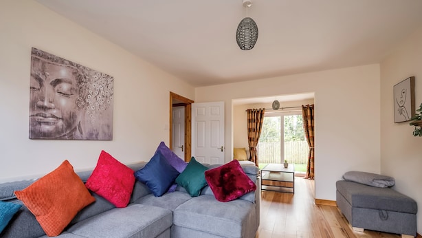 A modern living room with a grey sectional sofa, colorful cushions, a large abstract painting, and a wooden floor. - Stylish & spacious entire 3+1BR house in Lisburn(near Belfast)with parking  (Lisburn)