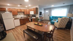 A modern kitchen with wooden cabinets, a dining table with benches, and a living area with a blue sofa and patterned armchair. - Charming 3 bedroom retreat (Herrin)