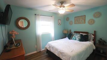 A bedroom with a bed, a ceiling fan, a TV, a dresser, and a window with curtains.
