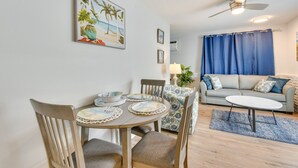 Ein Essbereich mit einem runden Tisch, Stühlen und einer dekorativen Mitte. Im Hintergrund befindet sich eine Couch und ein Deckenventilator.