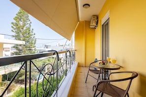 A balcony with a table and chairs, a window, and a view of buildings and trees.