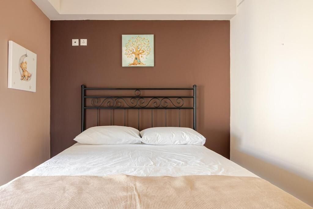 A bedroom with a bed, a wall-mounted picture of a tree, and a wall-mounted light switch.
