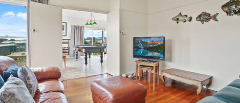 A living room with a pool table, leather sofas, a television, and decorative fish on the wall.
