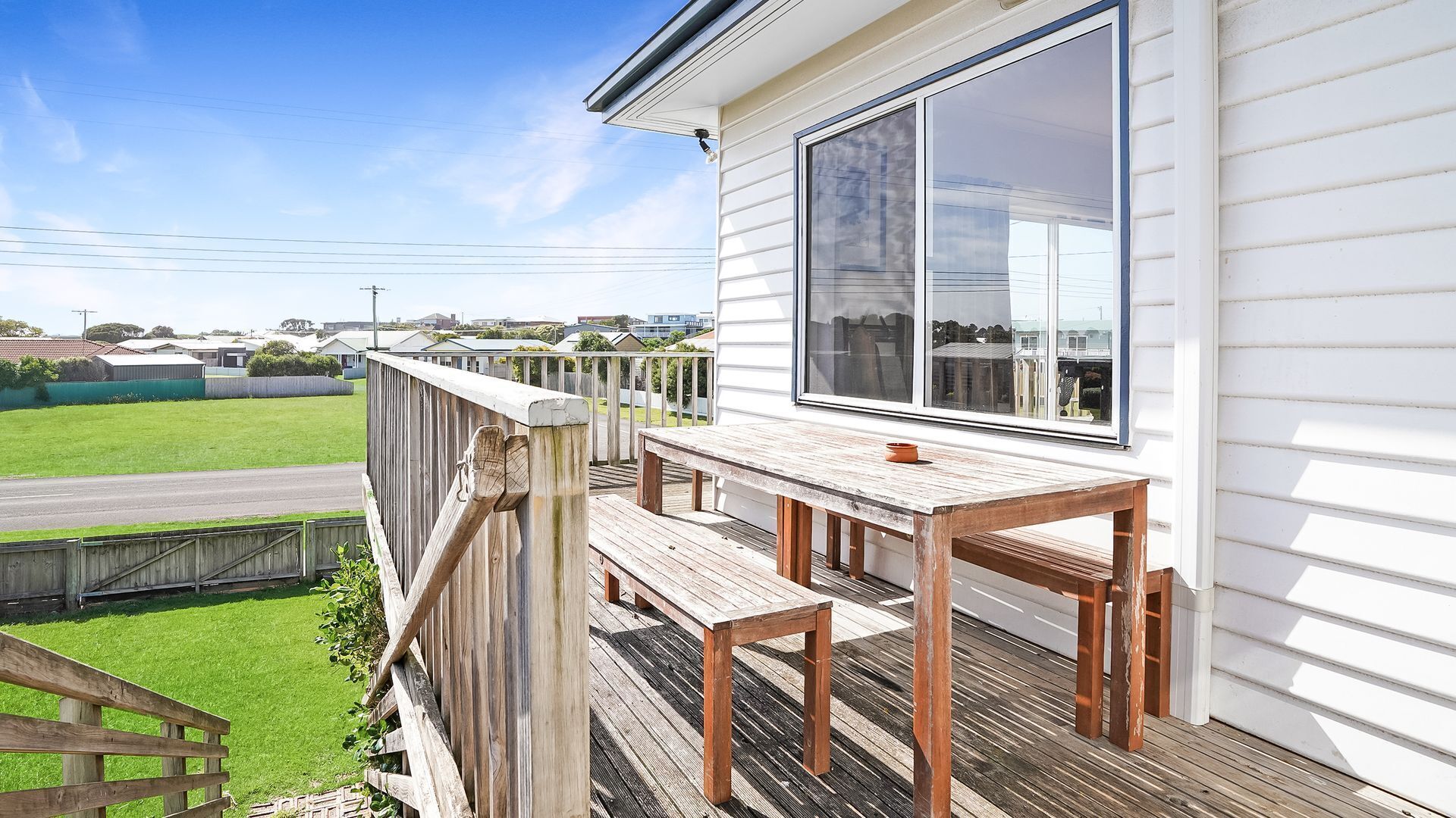 A wooden deck with a table and chairs, overlooking a residential area with houses and a road.