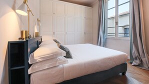 Een slaapkamer met een bed, nachtlampjes, een kledingkast en een raam met gordijnen.