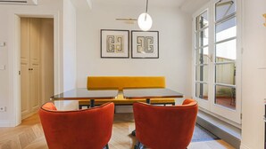Een eethoek met een tafel, twee stoelen, een bankje en twee kunstwerken aan de muur.