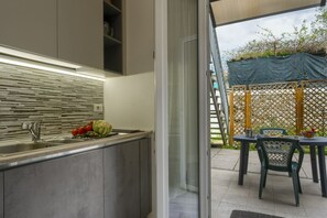 A modern kitchen with a built-in island, a sink, and a glass door leading to an outdoor patio area with a table and chairs.
