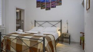Quarto com cama, mesa de cabeceira, luminária e uma obra de arte na parede, além de porta para o banheiro.