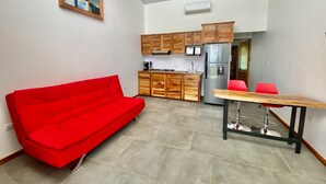Un espace de vie compact comprenant un coin cuisine, un canapé rouge et une table à manger.