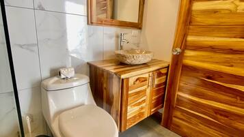 Et badeværelse med et marmortapet gulv, et hvidt toilet, en trækommode med en sten-vask og en trædør.