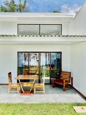 A patio with a wooden table and chairs, a glass door leading to a garden, and a white exterior wall. - 1bdr Condo 4 | SALAMANDRA in Uvita | 180° Ocean Views | Pool (Uvita)