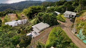 A hillside property with a swimming pool, a white building, and a view of the ocean. - 2bdr Condo 6 |RANA | Amazing sea view | Shared Infinity Pool (Uvita)