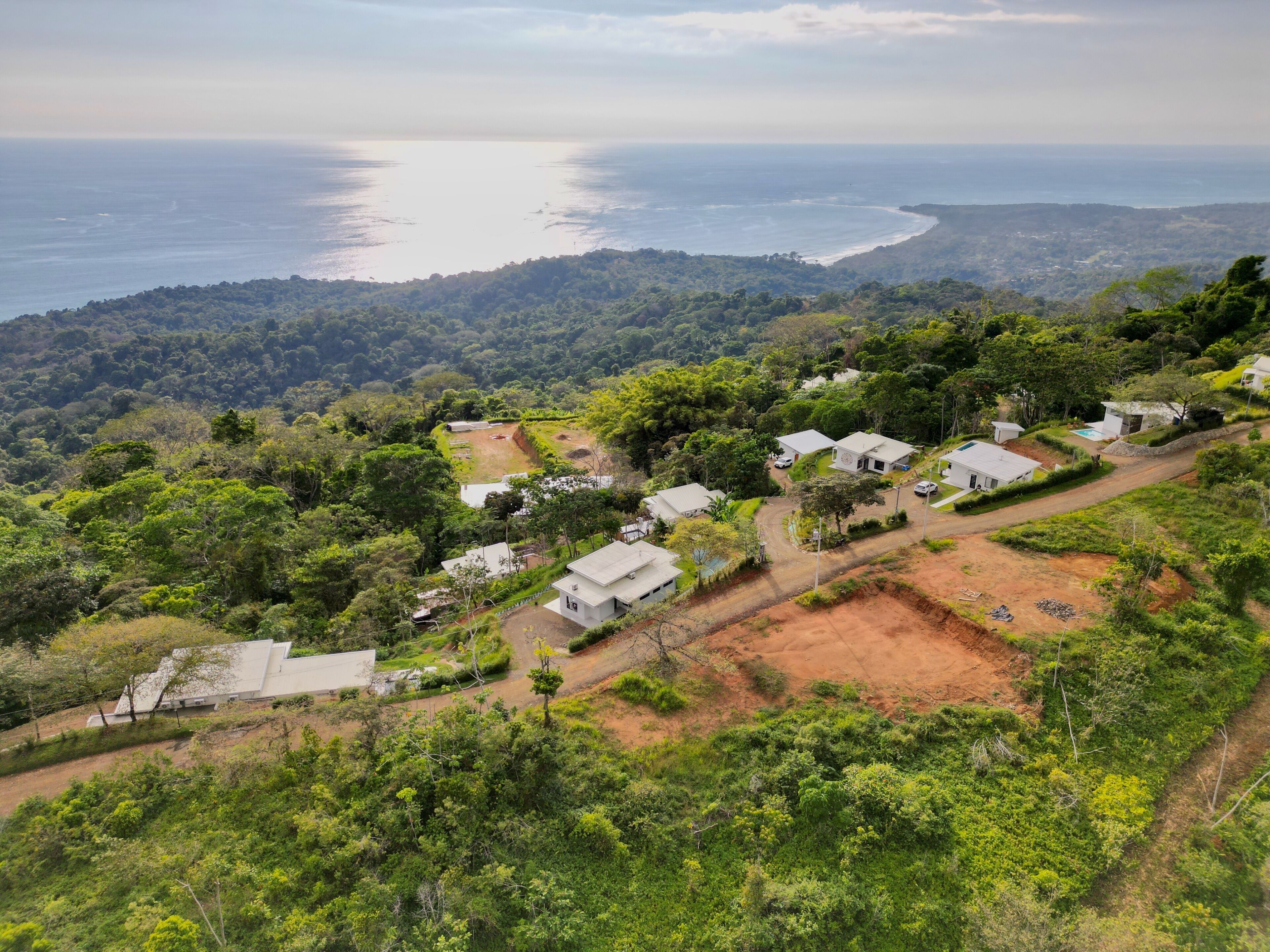 A hillside property with several white buildings, a dirt road, and a view of the ocean.