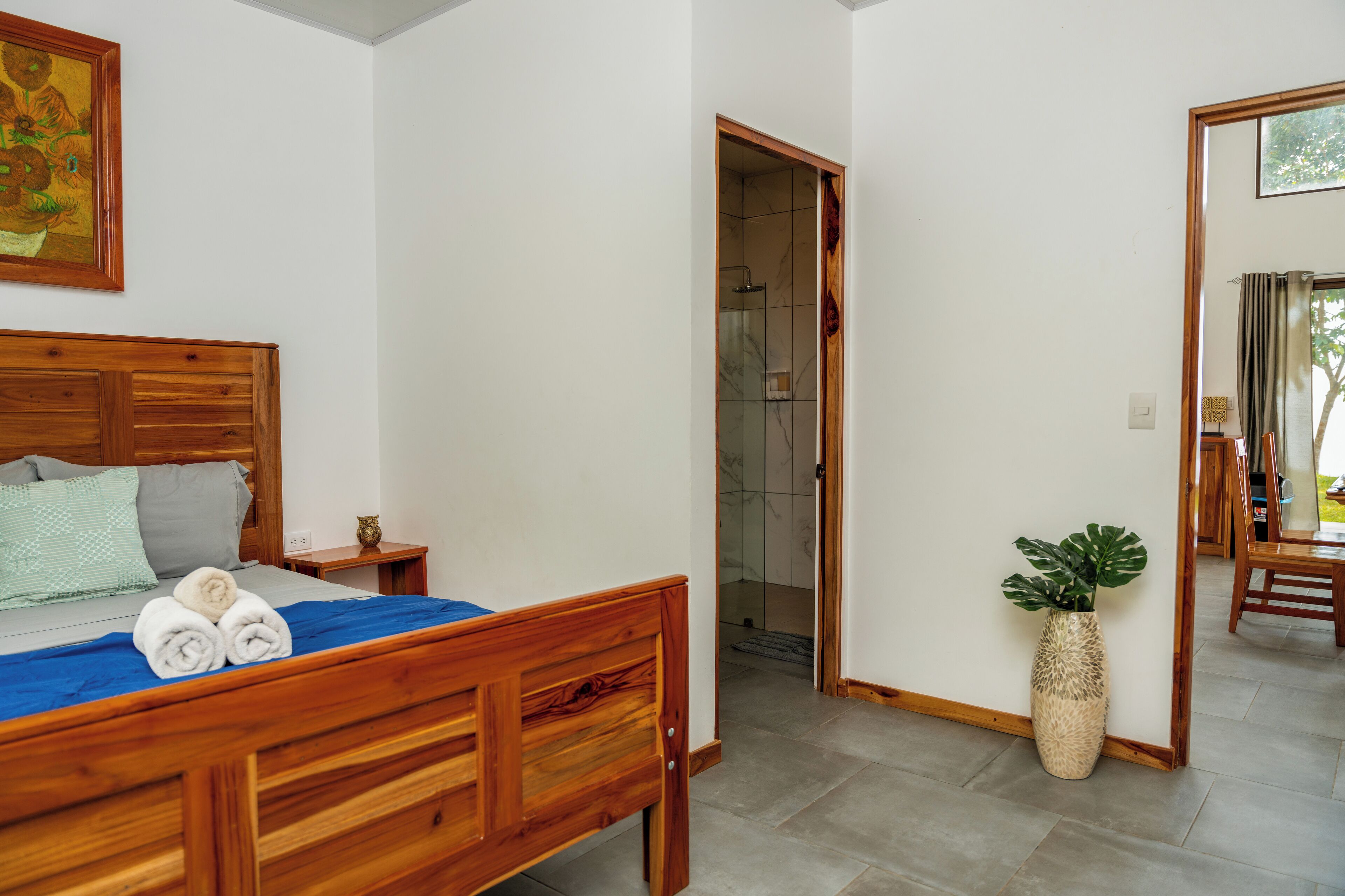 A bedroom with a wooden bed, a nightstand, a potted plant, and a shower area.