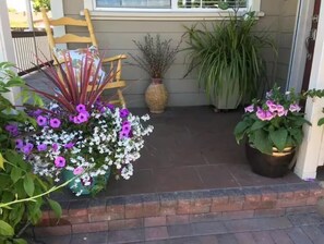 Un porche avec une chaise en bois, un pot de fleurs et une composition florale.