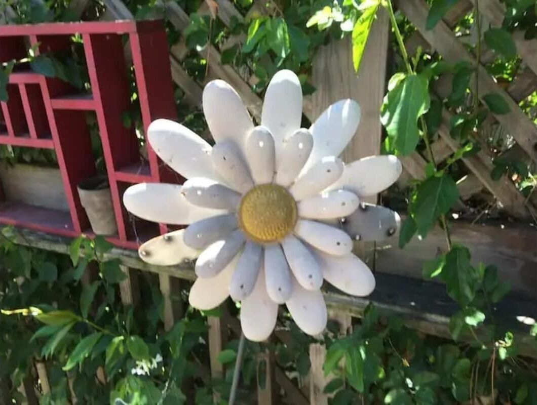A large artificial flower with a yellow center and white petals, surrounded by green foliage.
